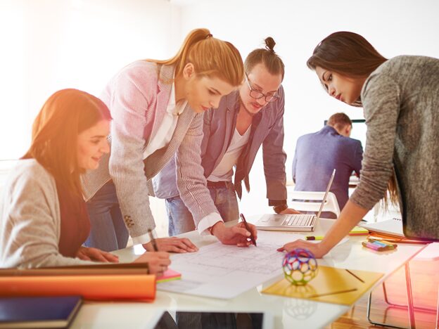 Four people gather around a desk while a woman marks a piece of paper