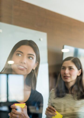 Four team members looking at a glass office wall with colorful post-it notes