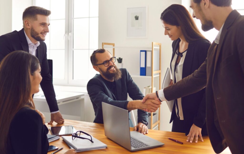 Professionals around a laptop shaking hands over PPM for enterprise discussions